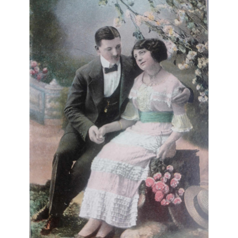 POSTAL PAREJA ANTIGUA SENTADA EN UN JARDÍN. COLOREADA.